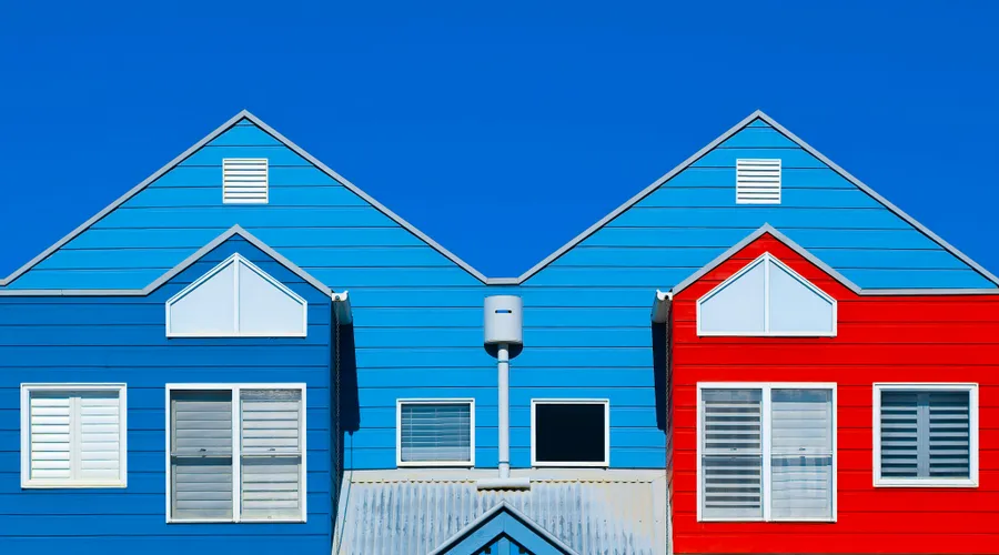 Head-to-Head: Durability & Weather Resistance - Brightly painted house facades in blue and red create a striking contrast against a clear blue sky